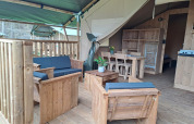 Tente safari avec sanitaires au Camping de Zeven Heuveltjes, dotée de meubles en bois et d'une terrasse couverte.