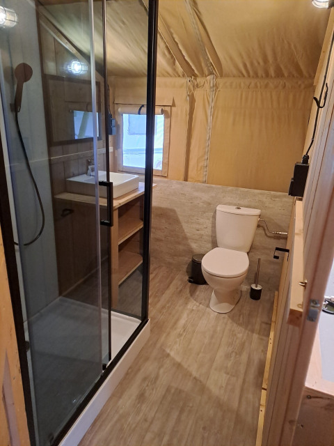 Vista interna di un bagno in tenda safari con doccia moderna, lavandino e WC, dettagli in legno.