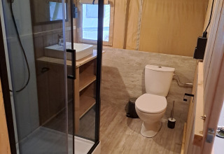 Interior view of a safari tent bathroom featuring a modern shower, sink, toilet, and wooden accents.