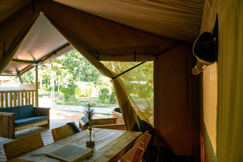 Interior view of a safari tent with wooden furniture and an outdoor green view at Campsite de Zeven Heuveltjes.