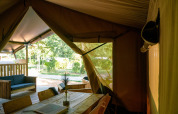 Interior view of a safari tent with wooden furniture and an outdoor green view at Campsite de Zeven Heuveltjes.