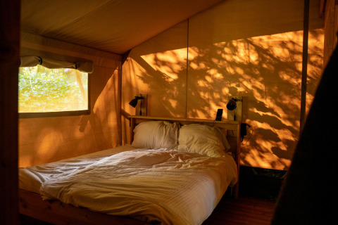 Cozy bed inside a safari tent at Campsite de Zeven Heuveltjes, Netherlands, with warm sunlight on the walls.