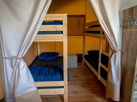 Foto de un área para dormir en una tienda safari con dos literas, ropa de cama azul y suelo de madera.