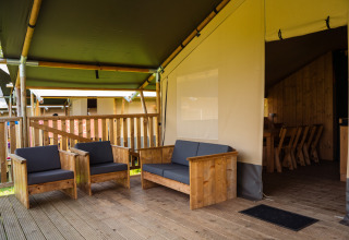Area salotto esterna con sedie in legno al Safaritent + servizi igienici al Camping de Chênefleur, Belgio.