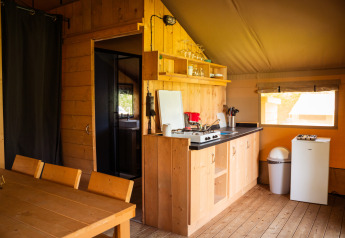 Interior de una tienda safari con mesa de comedor de madera, cocina pequeña, nevera y ventana.