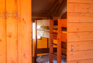 Interno di una tenda safari con letti a castello in legno e pareti in legno, illuminata da luce calda.