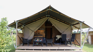 Tente safari avec sanitaires, terrasse en bois et fauteuils, située dans un environnement verdoyant.