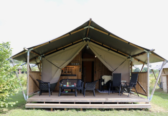 Safari tent with sanitary facilities, a wooden porch, and outdoor seating, set in a lush green environment.