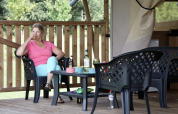 Donna che si gode una bevanda fuori dalla tenda Safari con servizi igienici al campeggio Heerlijkheid Vorenseinde, Paesi Bassi.