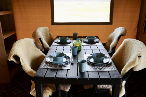 Mesa de comedor en tienda safari en Campsite de Heerlijkheid Vorenseinde, con vajilla azul y cubiertas de lana.