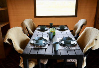 Dining table in Safari tent at Campsite de Heerlijkheid Vorenseinde, set with blue dishes and sheepskin covers.