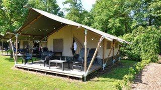 Tenda safari con veranda, arredi da esterno e un ambiente verde lussureggiante in una zona tranquilla.