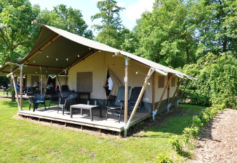 Safari-Zelt mit Veranda, Gartenmöbeln und grüner Umgebung, eingebettet in eine friedliche Naturkulisse.