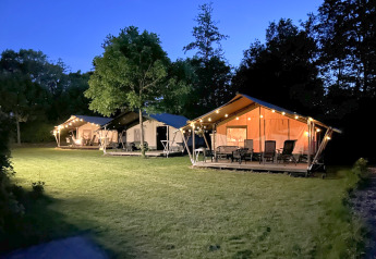 Safari-telte med terrasse og belysning ved aften på Campsite Emmen, Holland med grønne omgivelser.