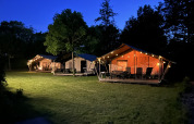 Safari tents with porches and string lights in the evening at Campsite Emmen, Netherlands, grassy area.