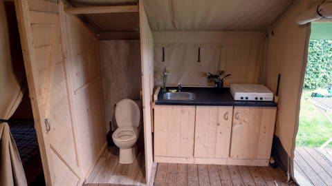Interieur van safaritent met toilet en keukenblok op Camping Emmen in Nederland, zicht op de tuin.