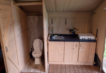 Interieur van safaritent met toilet en keukenblok op Camping Emmen in Nederland, zicht op de tuin.