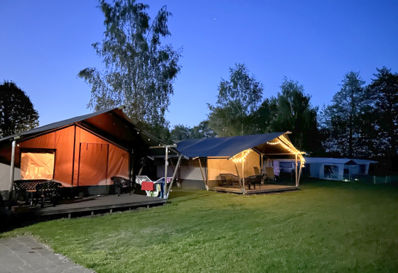 Avondfoto van een safaritent met toilet op Camping Emmen, Nederland, sfeervol verlicht en omgeven door bomen.