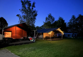 Evening view of a safari tent with toilet at Campsite Emmen, Netherlands, warmly lit and surrounded by trees.