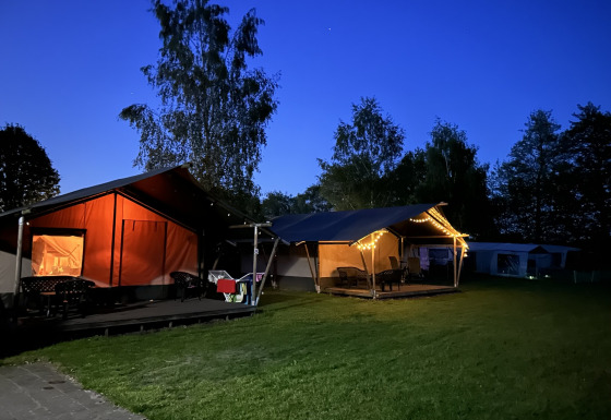 Aftenbillede af en oplyst safaritelt med toilet på Campingplads Emmen, Holland, omgivet af træer.