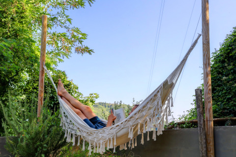 Person relaxing in a hammock with a book at the Safari tent at Campsite Pian D'Amora, Italy.