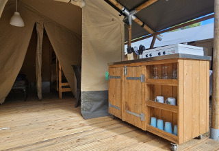 Vista interna di una tenda safari con pavimento in legno, cucina e mobili al campeggio Luna del Monte, Italia.