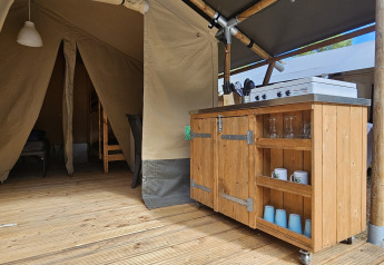 Interior view of a safari tent with wooden floor, kitchen unit and furniture at Campsite Luna del Monte, Italy.