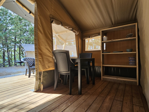 Vista interna di una tenda safari presso il campeggio Luna del Monte in Italia, con sedie, tavolo e scaffali.