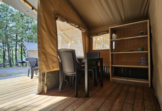Vista interna di una tenda safari presso il campeggio Luna del Monte in Italia, con sedie, tavolo e scaffali.