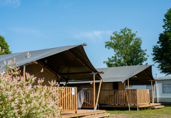 Safari tenten met houten veranda en sanitair, onder een blauwe lucht en omringd door bomen.