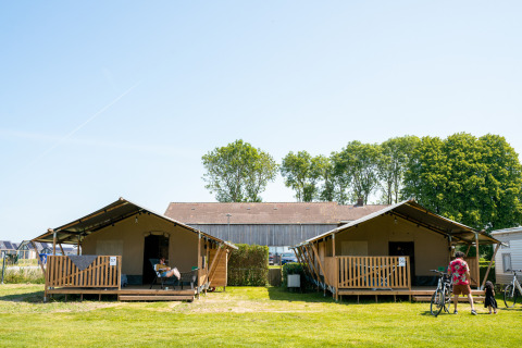 Deux tentes safari avec terrasses et vacanciers au camping Tussen de Diepen, Pays-Bas, journée ensoleillée.