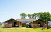 Two safari tents with decks and guests at Campsite Tussen de Diepen in the Netherlands, sunny day.