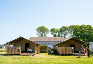 To safaritelt med terrasse og gæster på Campingplads Tussen de Diepen i Holland, solrig dag.
