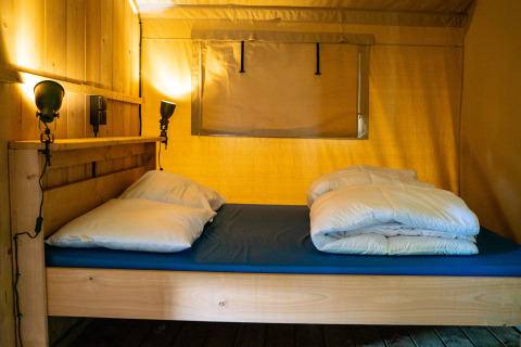 Double bed with white bedding inside safari tent with sanitary facilities at Campsite Tussen de Diepen, Netherlands.