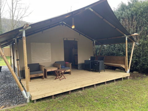 Tente safari avec terrasse en bois couverte, espace salon extérieur et meubles dans un cadre verdoyant.