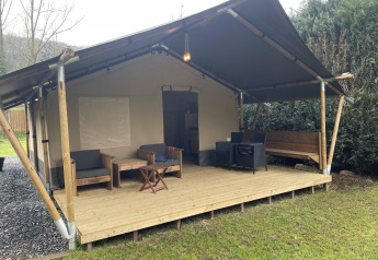 Safari tent with covered wooden deck, outdoor seating, and furniture, surrounded by lush greenery.
