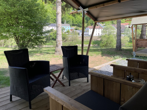 View from a safari tent terrace at Campsite du Rivage in Luxembourg with patio chairs and lush greenery.