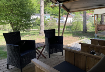 View from a safari tent terrace at Campsite du Rivage in Luxembourg with patio chairs and lush greenery.