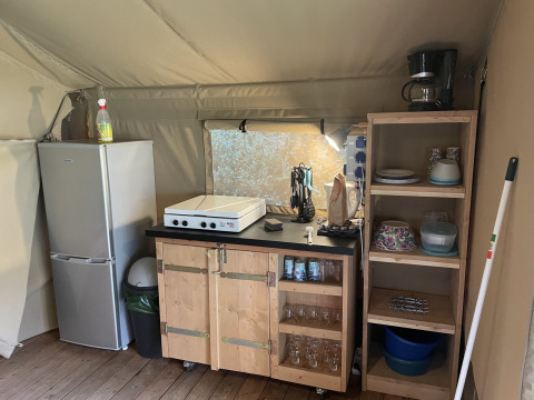 Petit coin cuisine dans une tente safari au Camping du Rivage avec réfrigérateur, étagères et plaque.