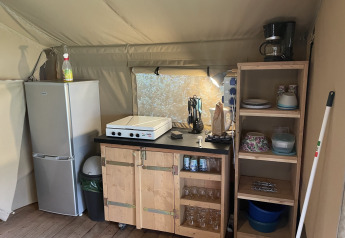 Petit coin cuisine dans une tente safari au Camping du Rivage avec réfrigérateur, étagères et plaque.