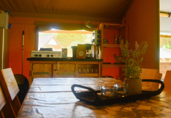 Interior of a safari tent with dining table and kitchen at Campsite du Rivage in Luxembourg.