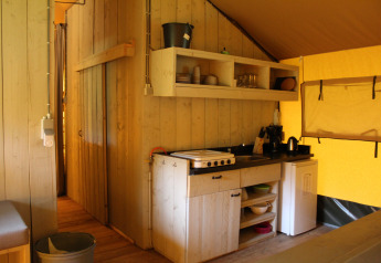Safari tent kitchen with wooden walls, shelves, stovetop, and mini fridge at Family park Goolderheide, Belgium.