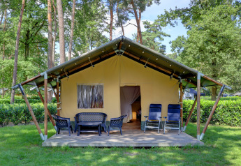 Safari-Zelt mit Terrasse, Gartenmöbeln und Liegestühlen im ruhigen, grünen Waldcampingplatz.