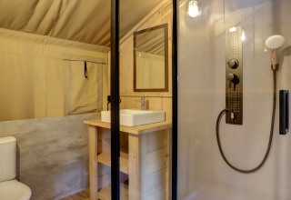 Interior of safari tent bathroom at Family park Goolderheide, Belgium, with shower, sink, and toilet visible.