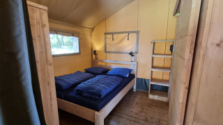 Habitación de tienda safari con cama doble, ropa de cama azul y muebles de madera en suelo de madera.
