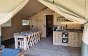 Interieur van safaritent met houten eettafel, stoelen, keuken en een gezellige, natuurlijke sfeer.