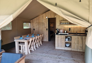 Intérieur d'une tente safari avec table à manger en bois, coin cuisine et ambiance chaleureuse en plein air.