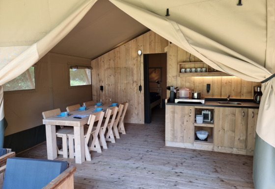 Intérieur d'une tente safari avec table à manger en bois, coin cuisine et ambiance chaleureuse en plein air.