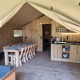 Innenraum eines Safarizeltes mit Holzmöbeln, Esstisch, Küche und gemütlicher Camping-Atmosphäre.