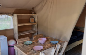 Vue intérieure d'une tente safari avec salle à manger en bois rustique et éclairage doux.